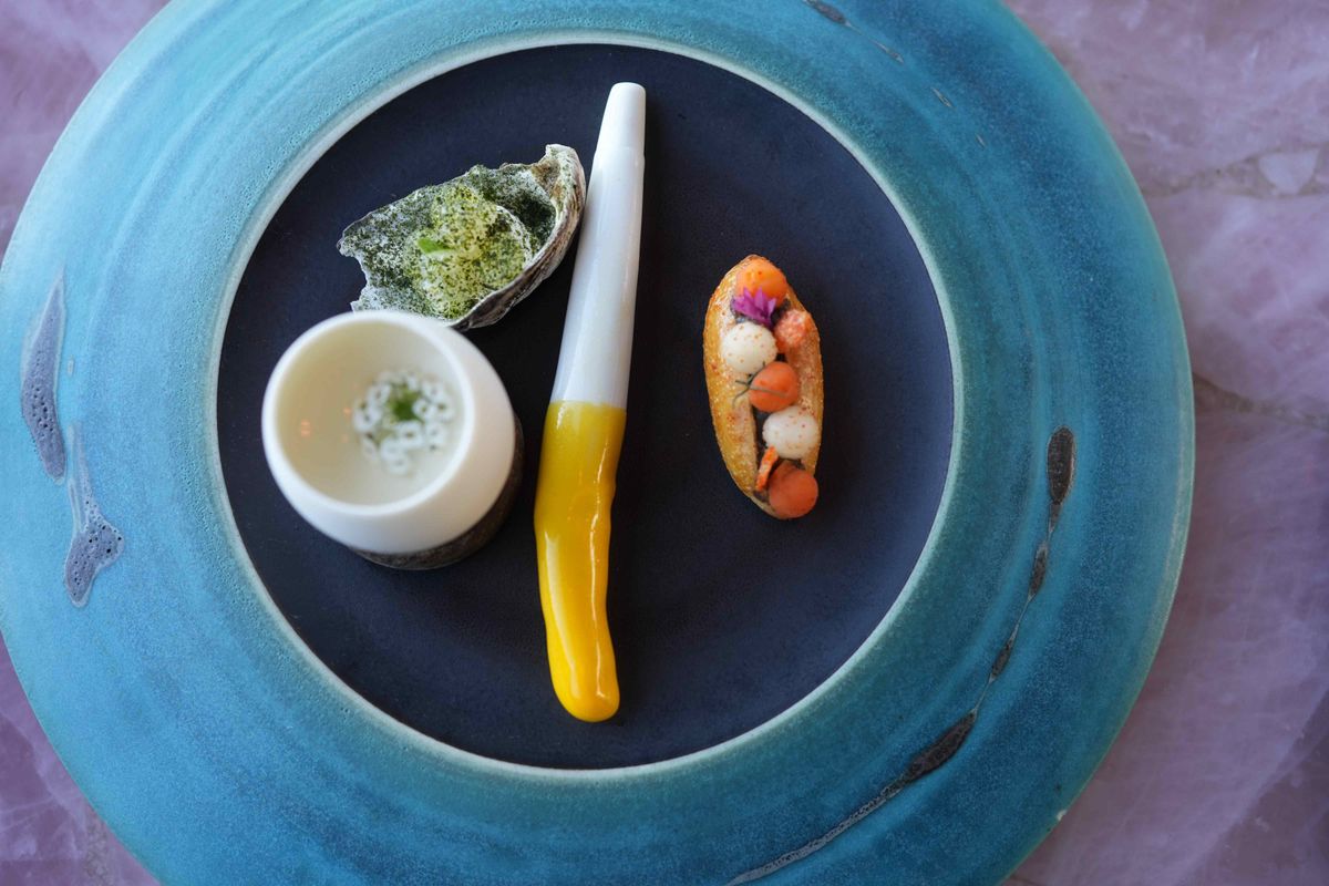 「FUCK ART LET’S EAT」という過激な名前の前菜から始まるのがMONAらしい。左は「GUCCI OYSTER」。本物の牡蠣の味を、発酵きゅうりなどの“フェイク”素材で模倣するというコンセプトの料理。ブランドのフェイクを揶揄（やゆ）したもの。真ん中の「LICK THINE GOLDEN  DAIVID  WALSH’S FINGER」は、陶器でできた指形のオブジェにサフランとトマトのシートがまとわせてあり、左のオランデーズソースに浸してしゃぶって食べる。右はミニバインミー
